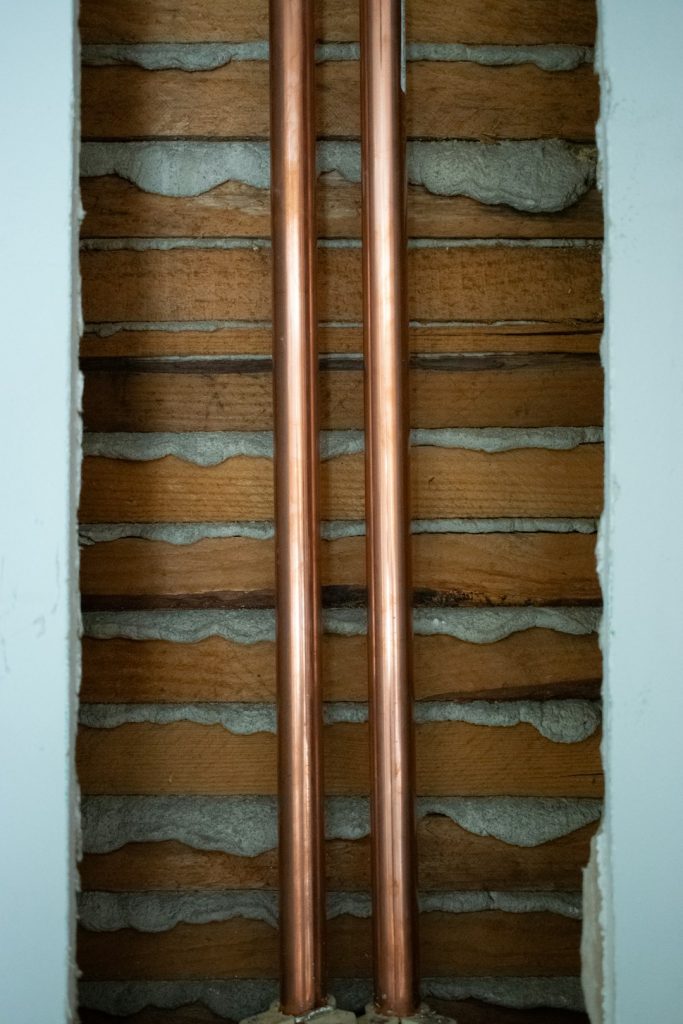 a-pair-of-copper-pipes-sitting-on-top-of-a-wall-c5aw5xy-o7c An insightful cutaway image showcases two vertical copper pipes, revealed within a torn away section of a wall. Surrounding plaster, lathe, and remnants of drywall give a raw, exposed look at the homes plumbing infrastructure. This photograph provides a detailed view into construction elements, particularly the world of plumbing, making it apt for topics related to home renovation, repair processes, and the inner workings of residential structures.